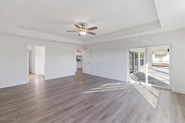 spare room with ceiling fan, wood-type flooring, and a tray ceiling