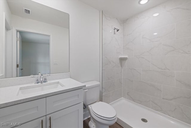 bathroom featuring vanity, a tile shower, and toilet