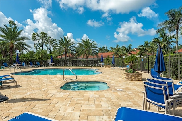 community pool with a patio area, fence, and a hot tub