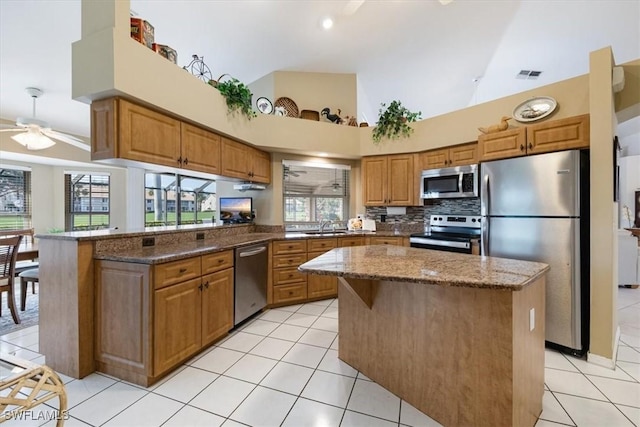 kitchen with stainless steel appliances, a peninsula, a kitchen island, visible vents, and dark stone countertops