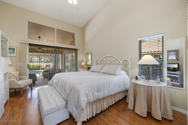 bedroom featuring access to exterior, high vaulted ceiling, baseboards, and wood finished floors