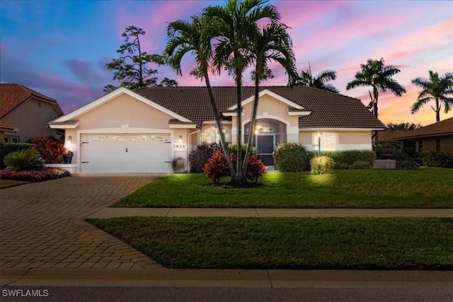 ranch-style house featuring a garage, a front lawn, decorative driveway, and stucco siding