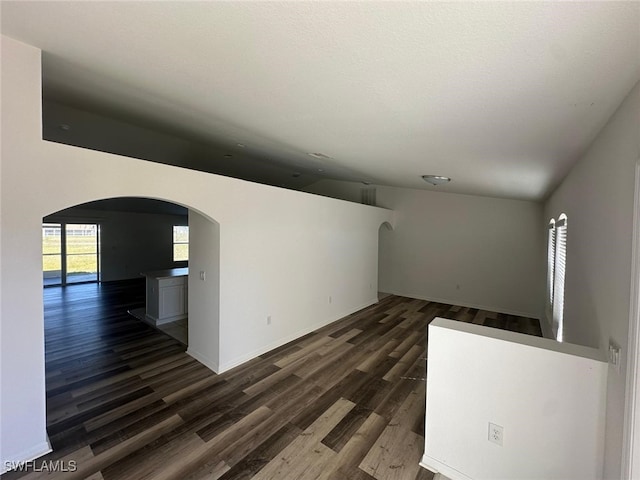 unfurnished living room featuring dark wood-type flooring, lofted ceiling, and a textured ceiling