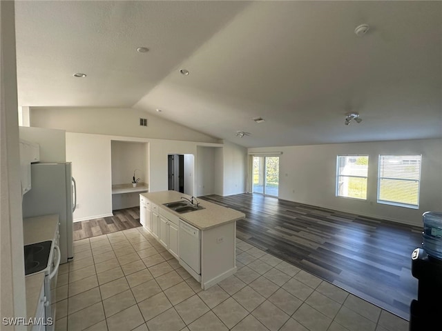 kitchen featuring sink, white appliances, light tile patterned floors, white cabinets, and a center island with sink