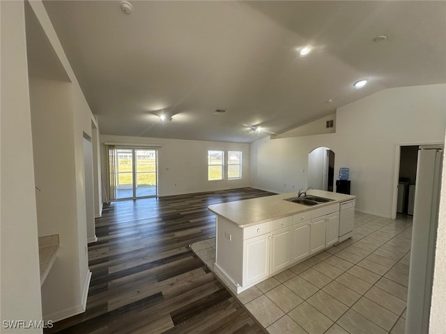 kitchen featuring sink, light hardwood / wood-style floors, white cabinets, a center island with sink, and vaulted ceiling