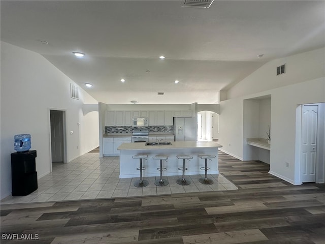 kitchen with white appliances, a kitchen breakfast bar, an island with sink, white cabinets, and decorative backsplash