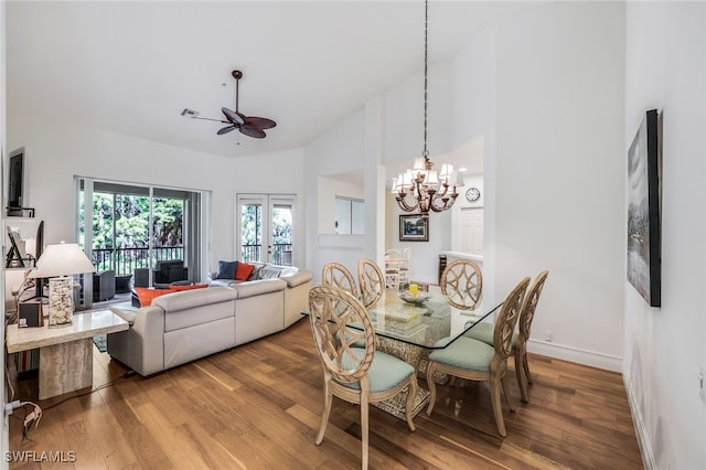 dining area with ceiling fan with notable chandelier, hardwood / wood-style floors, high vaulted ceiling, and french doors