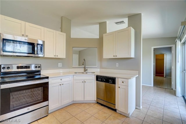 kitchen with light tile patterned flooring, appliances with stainless steel finishes, white cabinetry, lofted ceiling, and sink