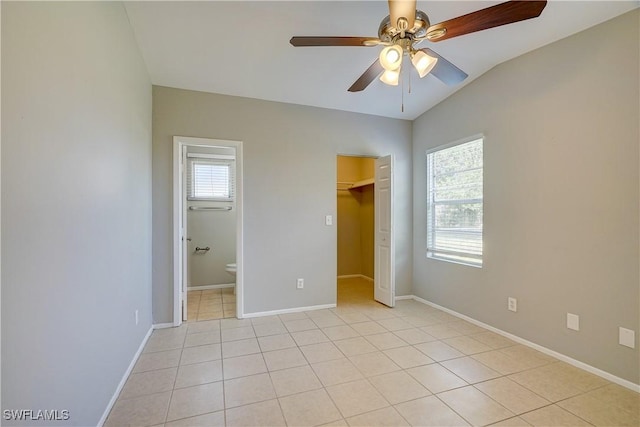 unfurnished bedroom featuring lofted ceiling, light tile patterned floors, connected bathroom, and ceiling fan