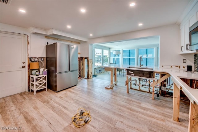 kitchen with white cabinets, freestanding refrigerator, light countertops, light wood-type flooring, and a sink