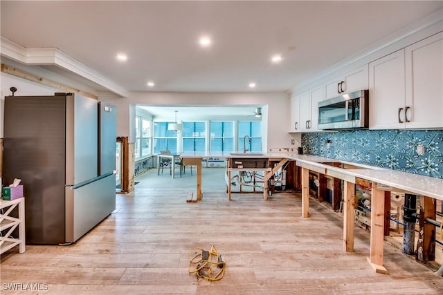 kitchen with white cabinetry, sink, backsplash, stainless steel appliances, and light hardwood / wood-style flooring