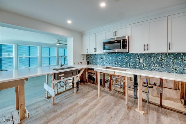 kitchen featuring tasteful backsplash, stainless steel microwave, light wood-style flooring, white cabinets, and a sink