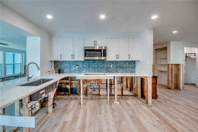 kitchen with tasteful backsplash, stainless steel microwave, a sink, and light wood finished floors