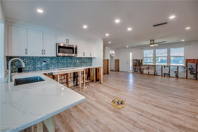 kitchen featuring sink, light stone counters, light hardwood / wood-style floors, decorative backsplash, and white cabinets