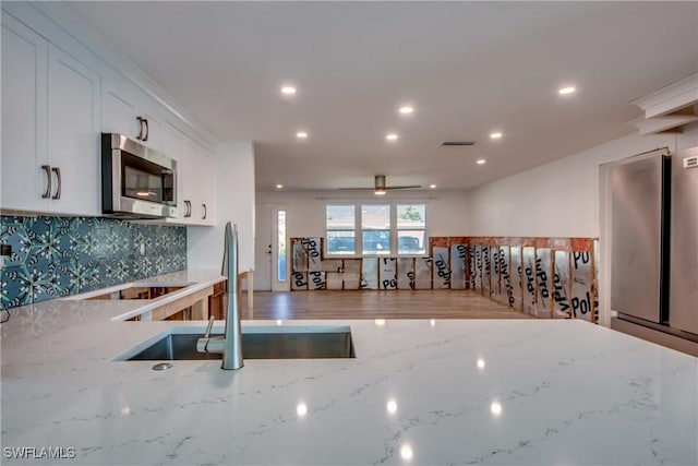 kitchen featuring sink, white cabinetry, light stone counters, wood-type flooring, and decorative backsplash