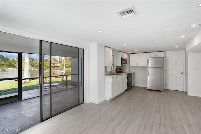 kitchen featuring stainless steel appliances, light hardwood / wood-style floors, white cabinets, and a water view