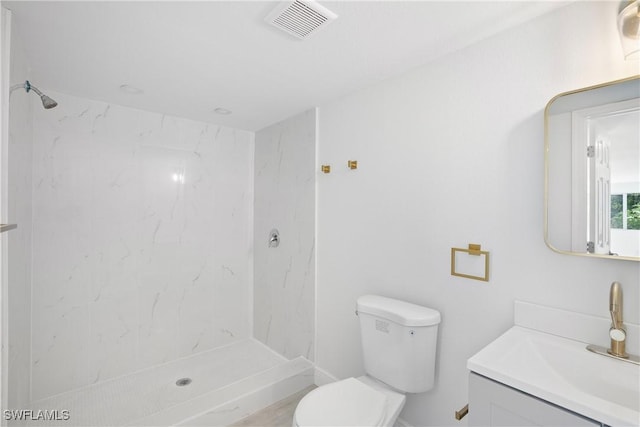 bathroom featuring vanity, a tile shower, and toilet