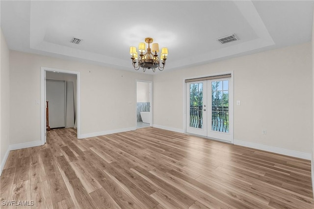 unfurnished room with an inviting chandelier, a tray ceiling, french doors, and light wood-type flooring