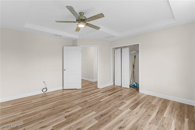 unfurnished bedroom featuring a raised ceiling, a closet, ceiling fan, and light hardwood / wood-style flooring