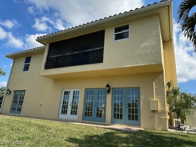 rear view of house featuring french doors, a balcony, and a lawn