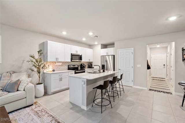 kitchen with sink, white cabinetry, a kitchen breakfast bar, stainless steel appliances, and an island with sink