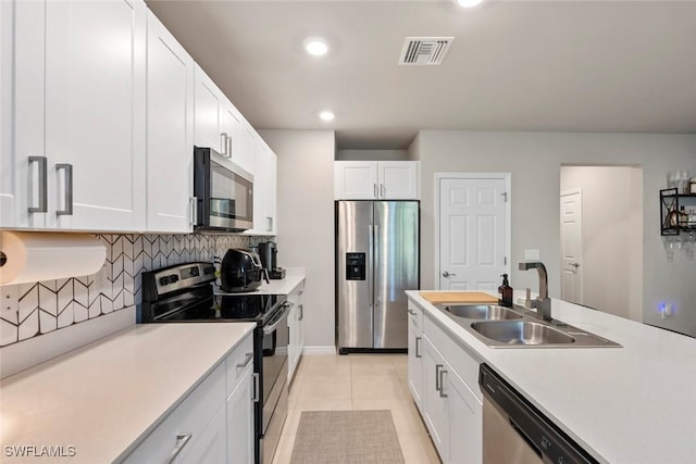 kitchen featuring appliances with stainless steel finishes, tasteful backsplash, sink, white cabinets, and light tile patterned floors