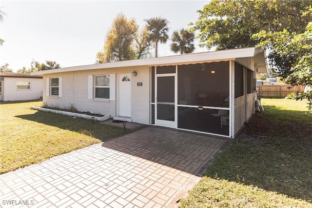 back of property with a sunroom, a patio, and a lawn