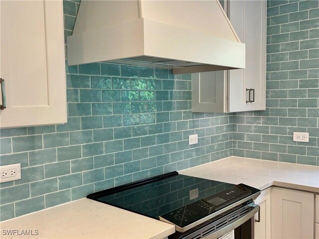 kitchen featuring electric stove, white cabinetry, decorative backsplash, and premium range hood