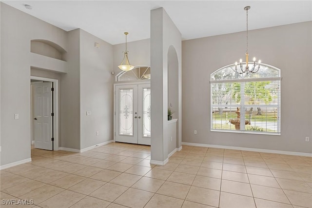 foyer with a towering ceiling, light tile patterned floors, a chandelier, and french doors