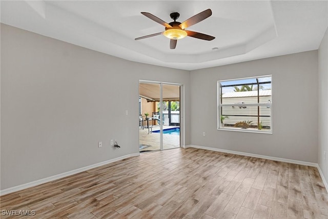 spare room with a tray ceiling, light hardwood / wood-style flooring, and ceiling fan