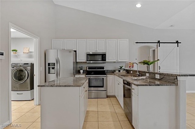 kitchen with appliances with stainless steel finishes, washer / clothes dryer, sink, dark stone countertops, and a barn door