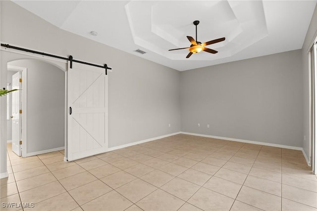 tiled empty room featuring ceiling fan, a tray ceiling, and a barn door