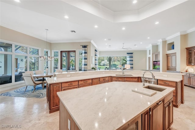 kitchen with sink, crown molding, a spacious island, light stone countertops, and decorative light fixtures