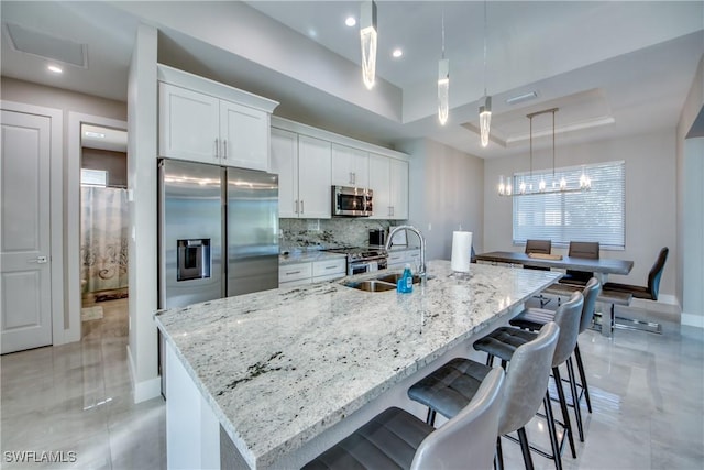 kitchen featuring white cabinetry, an island with sink, sink, stainless steel appliances, and a raised ceiling