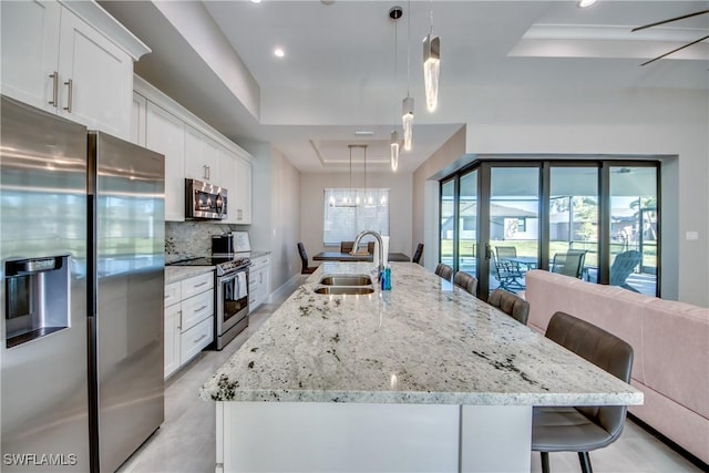 kitchen featuring appliances with stainless steel finishes, decorative light fixtures, sink, a kitchen island with sink, and a raised ceiling