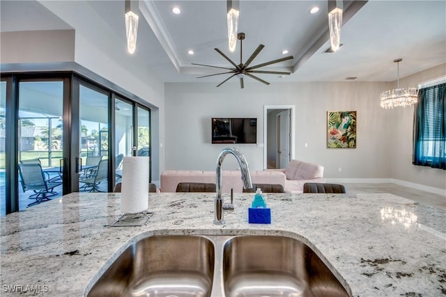 kitchen with a raised ceiling, sink, light stone counters, and an inviting chandelier