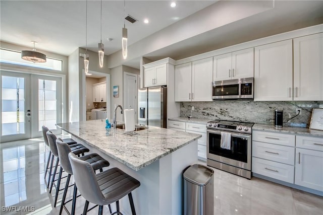 kitchen with pendant lighting, sink, white cabinetry, stainless steel appliances, and a center island with sink