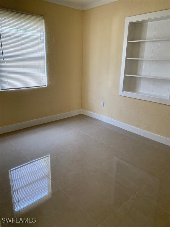 tiled spare room with built in shelves and ornamental molding