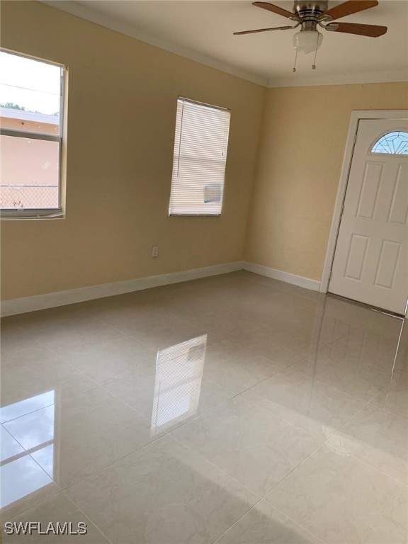 tiled empty room featuring ornamental molding and ceiling fan