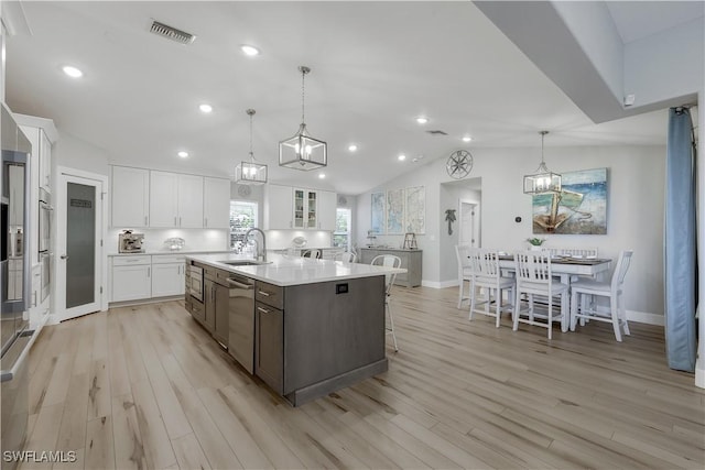 kitchen with decorative light fixtures, sink, white cabinets, light hardwood / wood-style floors, and a center island with sink