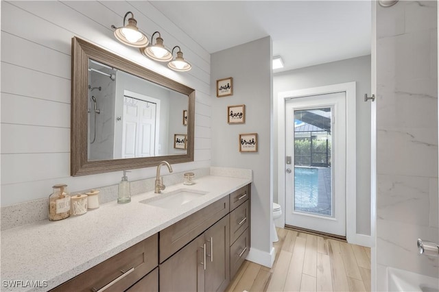 bathroom with hardwood / wood-style flooring, wooden walls, vanity, and toilet