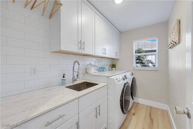 clothes washing area featuring cabinets, sink, washing machine and clothes dryer, and light wood-type flooring