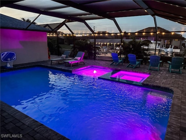 pool at dusk featuring an in ground hot tub, a lanai, and a patio