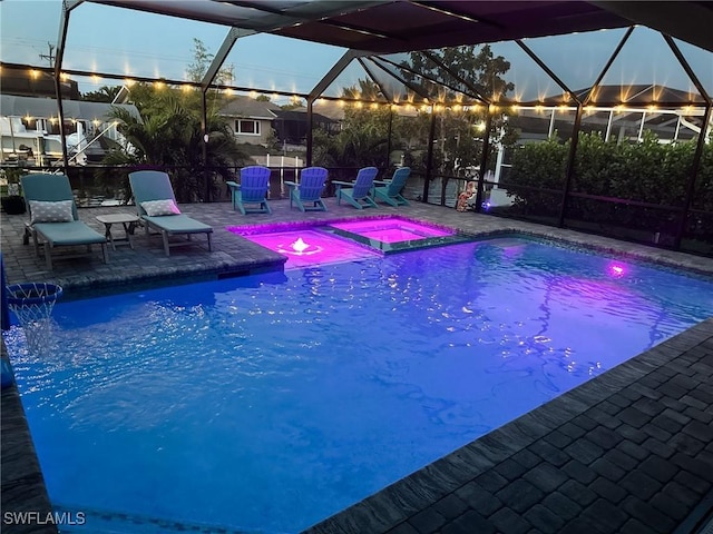 pool at dusk featuring an in ground hot tub, glass enclosure, and a patio