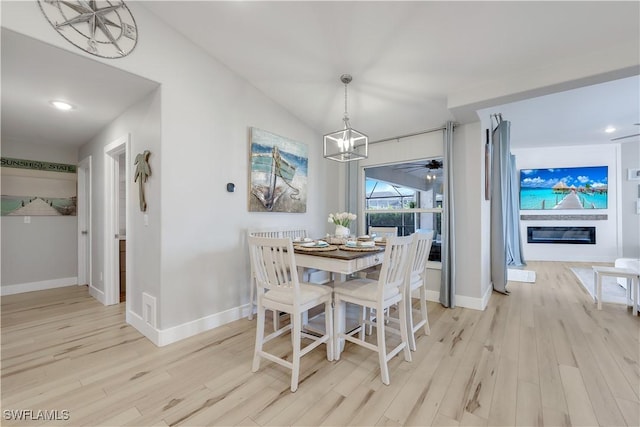 dining space featuring ceiling fan with notable chandelier, vaulted ceiling, and light hardwood / wood-style floors