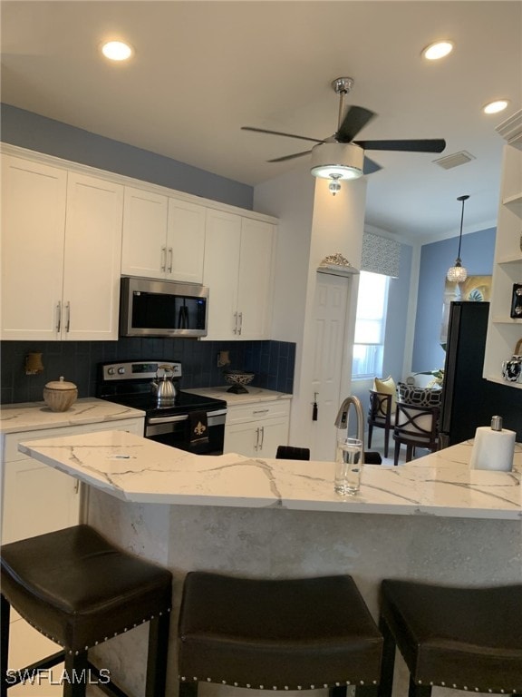 kitchen with vaulted ceiling, appliances with stainless steel finishes, white cabinets, a kitchen breakfast bar, and light stone countertops