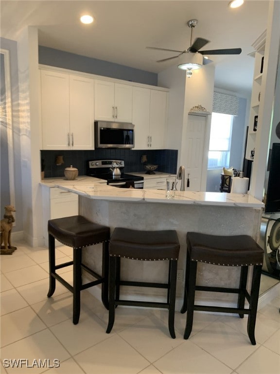 kitchen featuring light tile patterned flooring, white cabinetry, tasteful backsplash, appliances with stainless steel finishes, and a kitchen breakfast bar