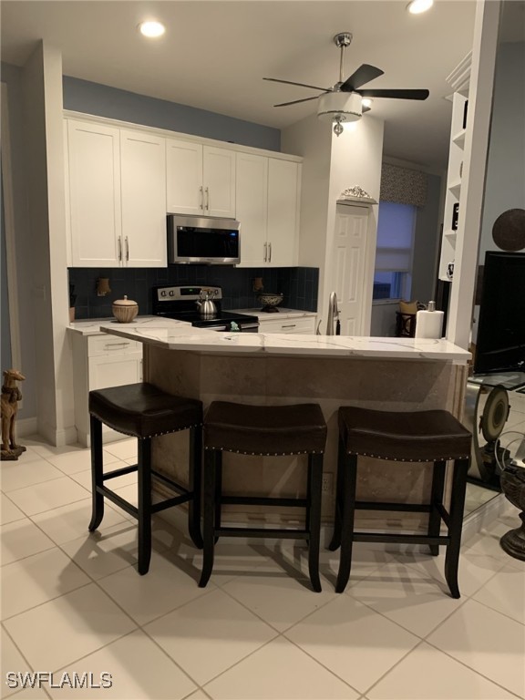 kitchen with stainless steel appliances, a kitchen breakfast bar, decorative backsplash, and white cabinets