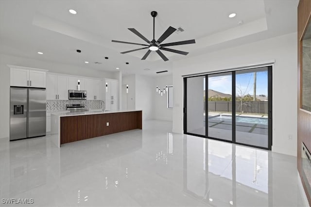 kitchen with stainless steel appliances, a kitchen island with sink, white cabinets, and a tray ceiling