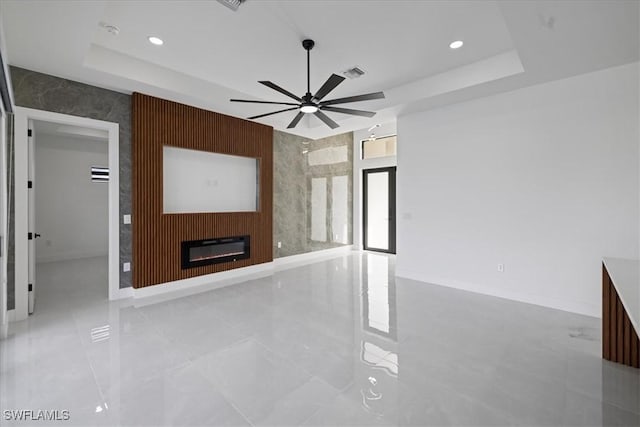 unfurnished living room featuring ceiling fan, a large fireplace, and a raised ceiling